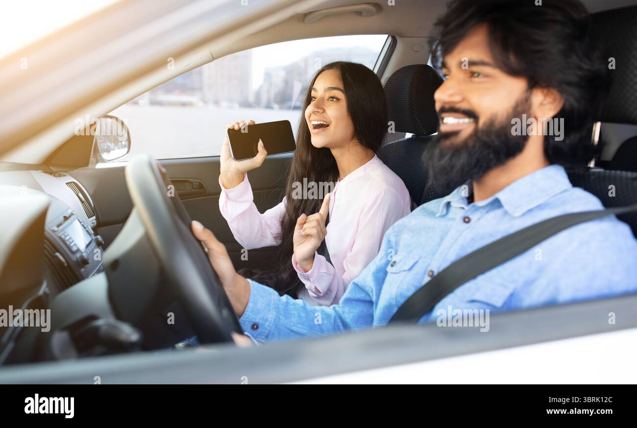 Indianerin singt mit Smartphone, während ihr Freund Auto fährt Stockfoto
