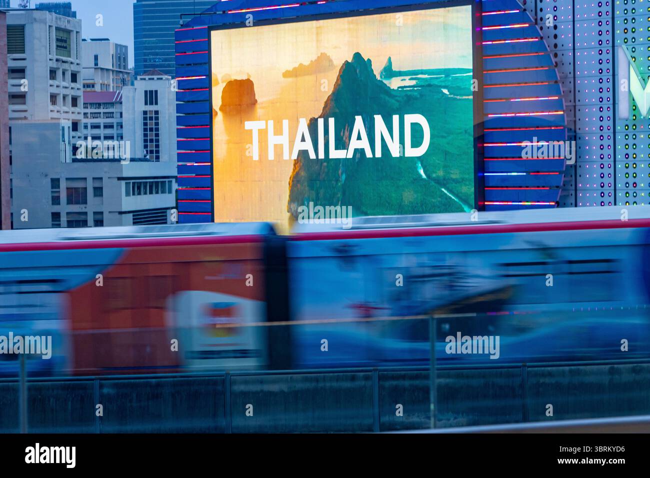 Verschwommene Stadtbahn vorbei an einer digitalen Werbetafel mit dem Wort „Thailand“ auf tropischem Hintergrund Stockfoto