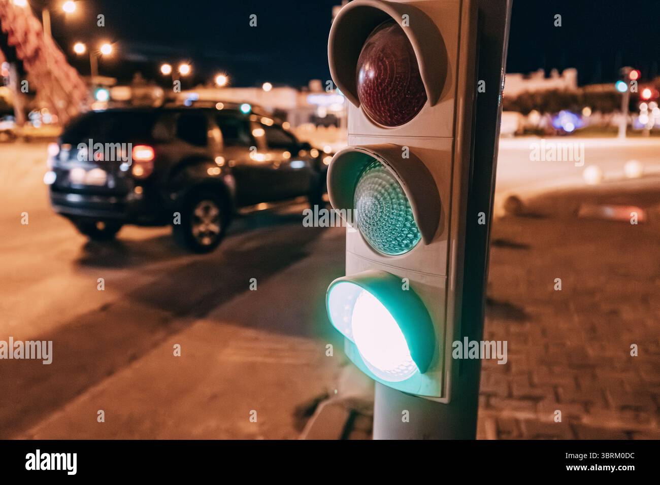 Grüne Ampel, die nachts leuchtet, mit verschwommenem Auto im Hintergrund, symbolisiert Verkehrsfluss und Straßensicherheit Stockfoto