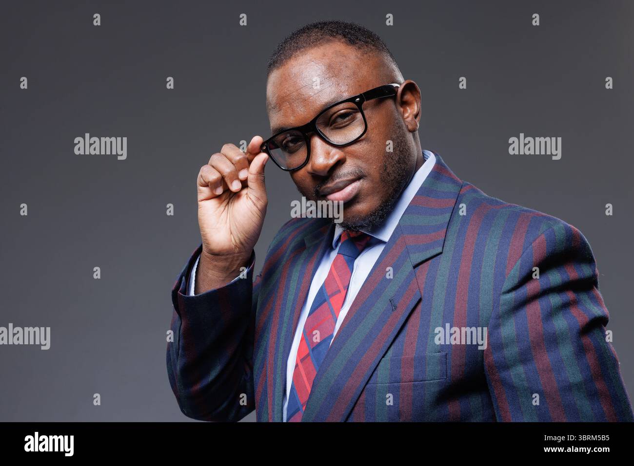 Selbstbewusster afrikanischer Geschäftsmann in moderner Brille und gestreiftem Anzug, der Stil, Erfolg und Führungsposition im Geschäft zeigt Stockfoto