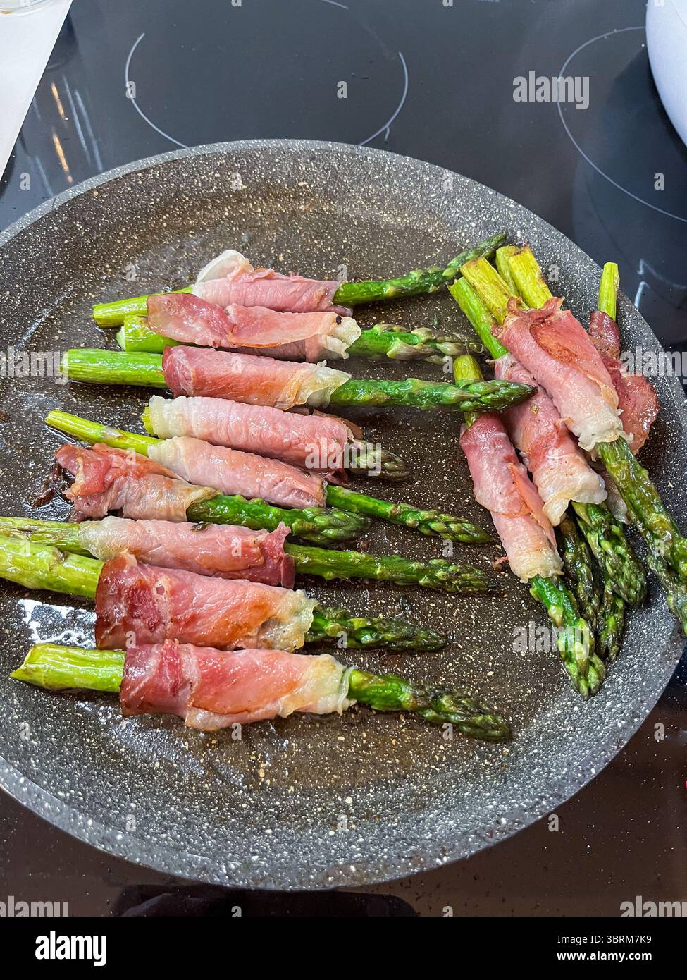 Spargelspeere in herzhaftes geräuchertes Fleisch gewickelt, wunderschön auf einer Pfanne angeordnet, um eine kulinarische Zubereitung für eine leckere Vorspeise oder Beilage hervorzuheben Stockfoto