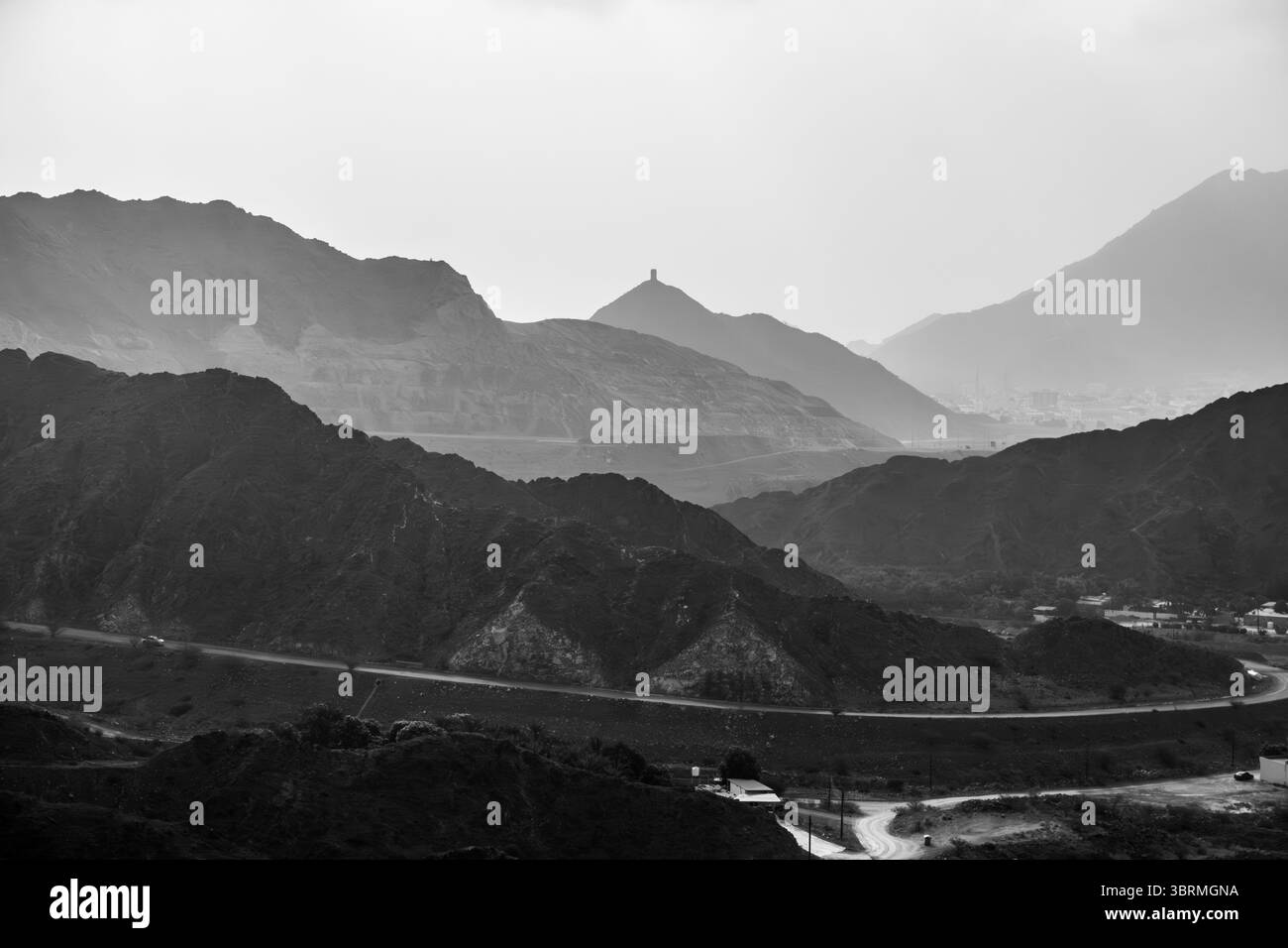 Nebelige Berglandschaft mit gewundener Straße und entferntem Turm, monochromem Ambiente, Schwarzweiß-Berglandschaft, Filmfotografie Stockfoto
