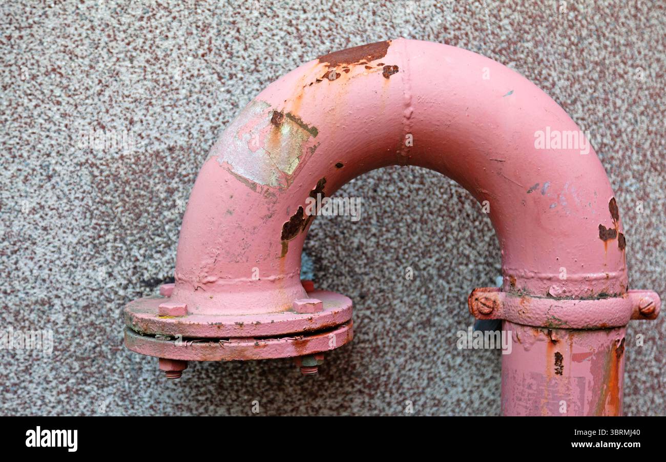 Ein gewölbter rosafarbener Industrierohranschluss mit rostigen Kanten und abblätternder Farbe auf einer strukturierten Betonoberfläche, der den Kontrast zwischen dem verdeutlicht Stockfoto
