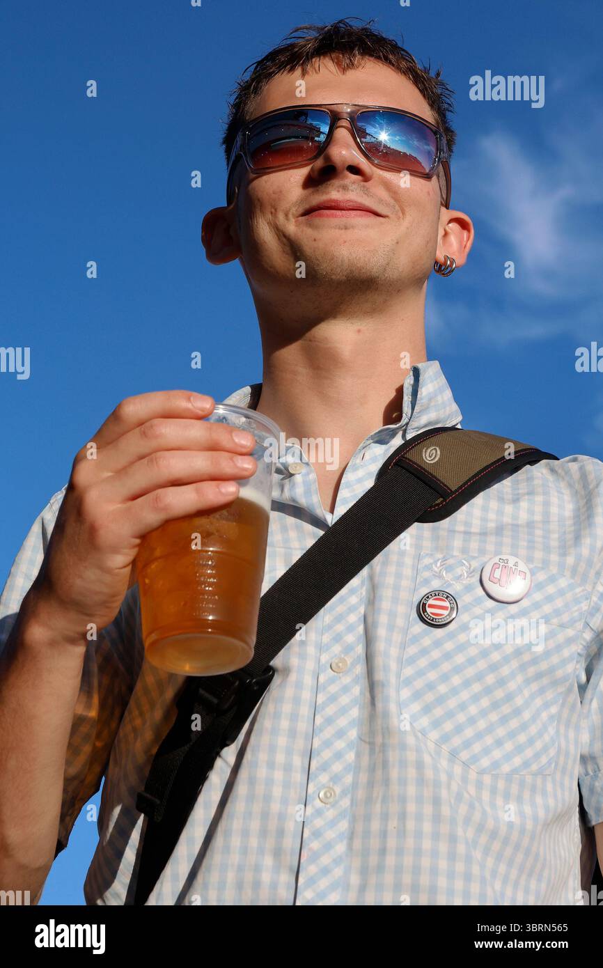 Ein junger Mann trinkt ein Pint Lager aus einem Plastikbecher Stockfoto
