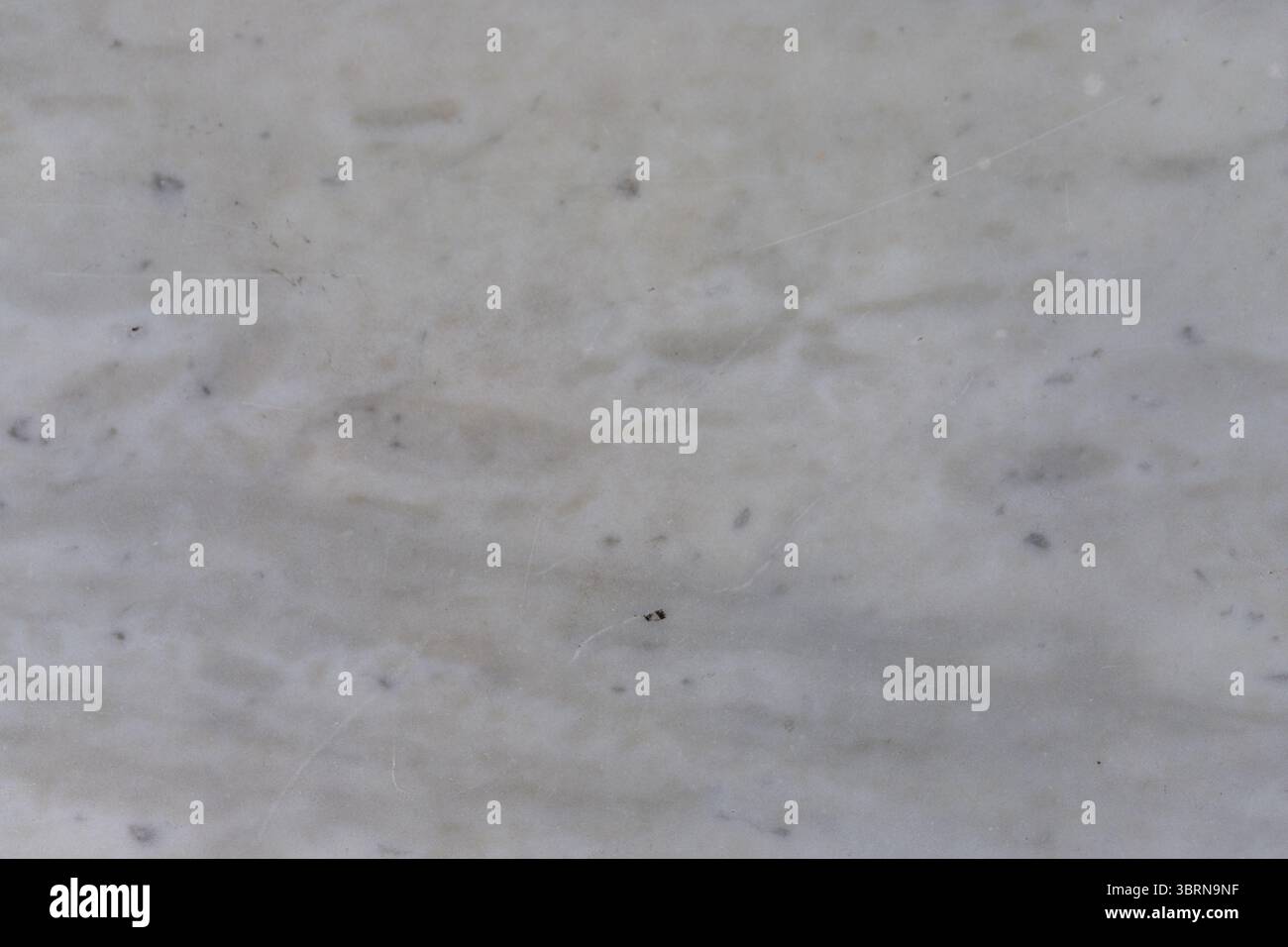 Nahaufnahme aus meliertem weißem und grauem Marmor mit dezenten Adern und kleinen dunklen Einschlüssen. Stockfoto