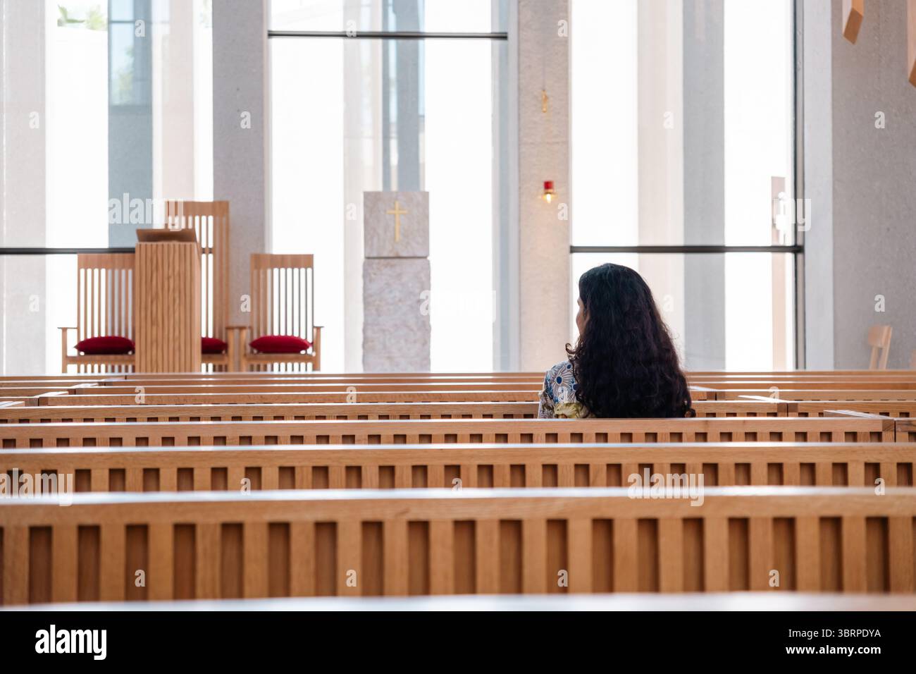 Eine junge Frau, die auf einer Kirchbank sitzt, gegenüber dem Altar Stockfoto
