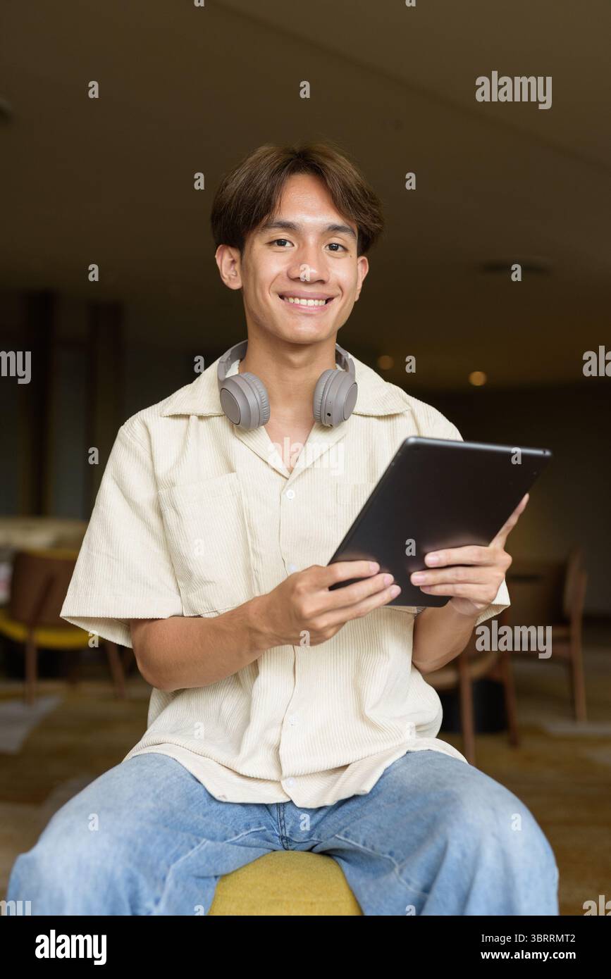Niedlicher asiatischer Studentenmann, der in einem modernen Café sitzt Stockfoto