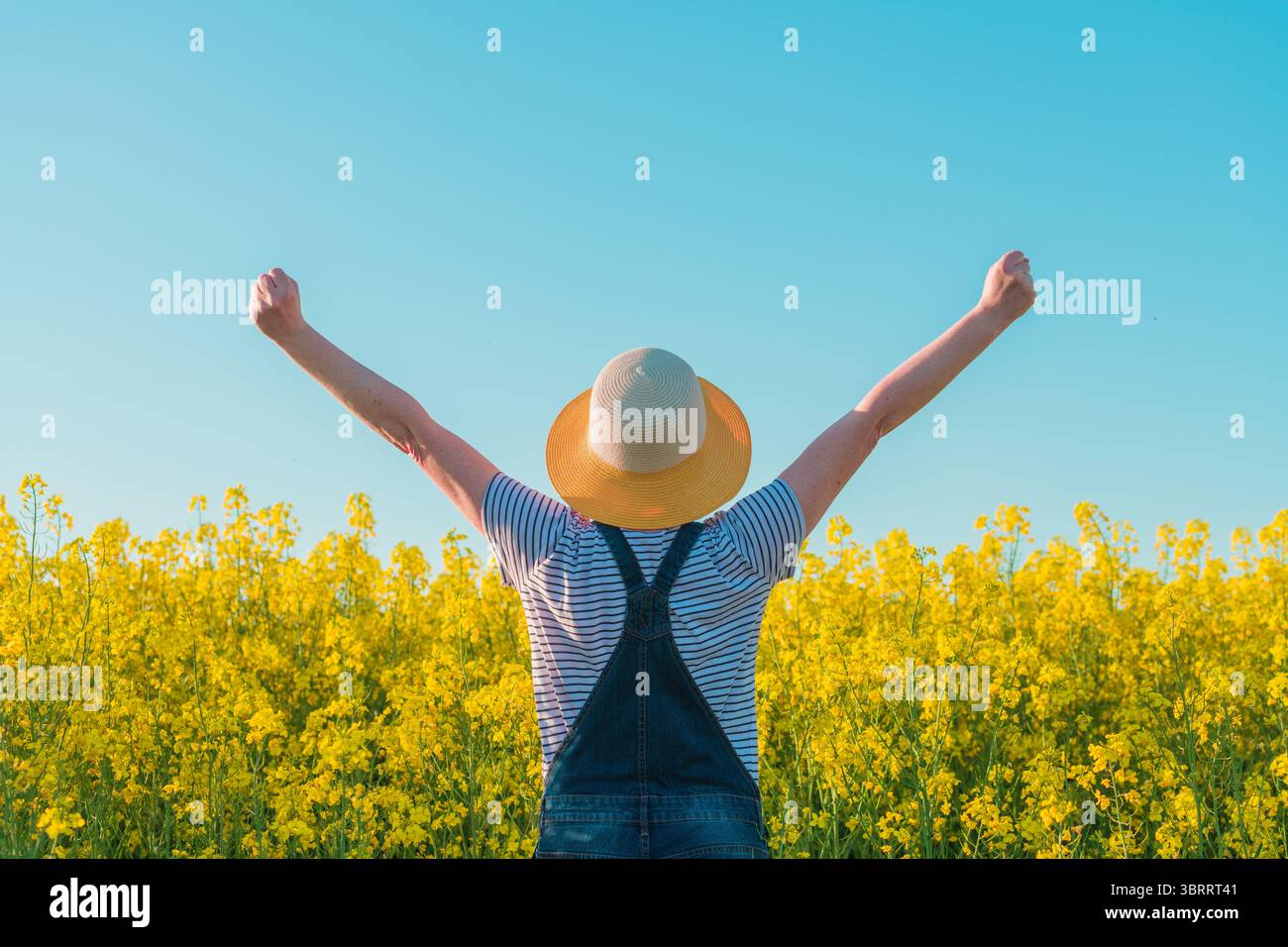 Erfolgreiche Landwirtin mit erhobenen Händen im Rapsfeld, selektiver Fokus Stockfoto