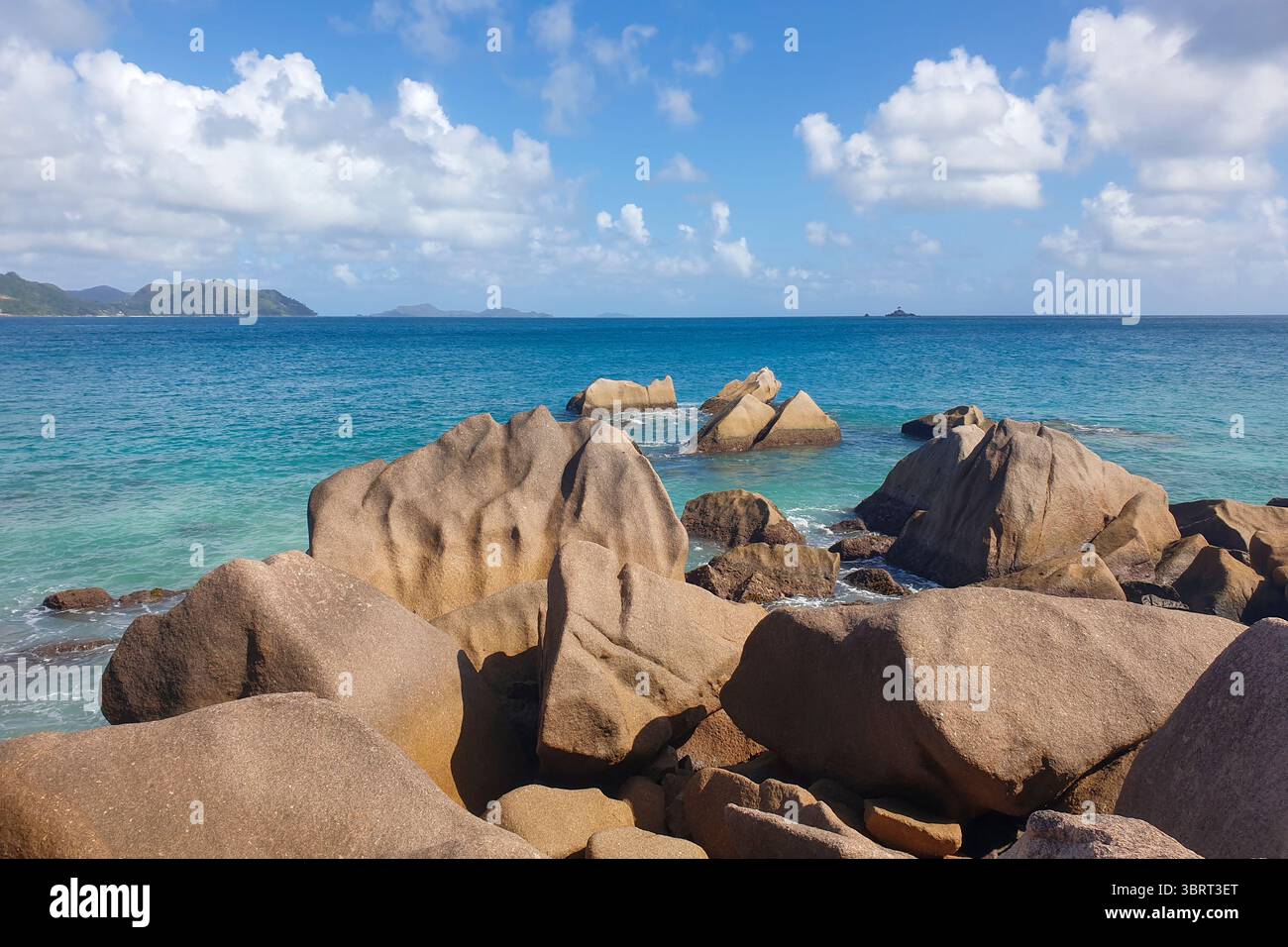 Große Granitfelsen und üppig grüne Bäume umrahmen das türkisfarbene Wasser am felsigen Ufer von Anse Strong auf La Digue Island. Stockfoto