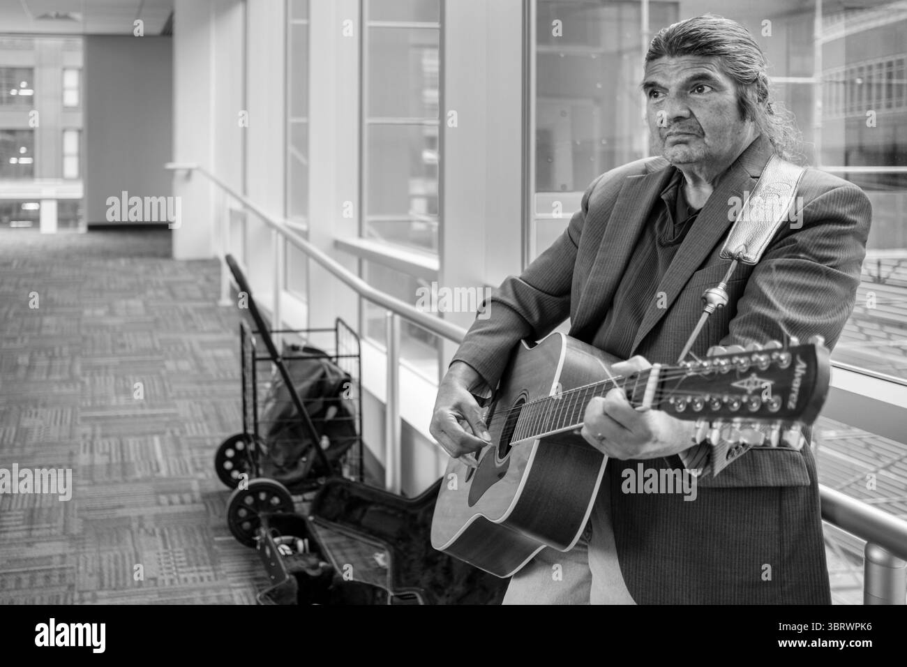 Oktober 2020, des Moines, Iowa, USA: RANDY KONG, ein Busker des Moines tritt in einem leeren Skywalk in der Innenstadt auf. Kong sagte, die Pandemie habe sein Einkommen verwüstet. Es gibt viel weniger Leute, die in der Innenstadt arbeiten, und diejenigen, die es sind, hören nicht auf, ihm zuzuhören oder Geld in seine Gitarrenhülle zu werfen. Die Wirtschaft in der Innenstadt des Moines spürt immer noch die Auswirkungen der im März angeordneten COVID-19-Abschaltung. Sieben Monate nach der Schließung haben Arbeitgeber ihre Arbeitnehmer immer noch von zu Hause aus zu arbeiten. Restaurants, Friseurläden und Einzelhandelsgeschäfte spüren die Auswirkungen. Viele haben Arbeitskräfte und Arbeitsstunden geschlossen oder gekürzt Stockfoto