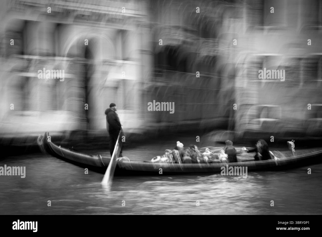 Eindringliches Schwarz-weiß-Bild eines Mannes, der eine Gondel auf dem großen Kanal mit einer Schädelmütze und einem langen Wintermantel paddelt, Menschen und Gepäck trägt Stockfoto