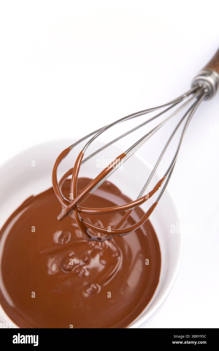 Konditorin, der geschmolzene Schokolade in einer Porzellanschale mit Schneebesen über der Sicht verrührt Stockfoto