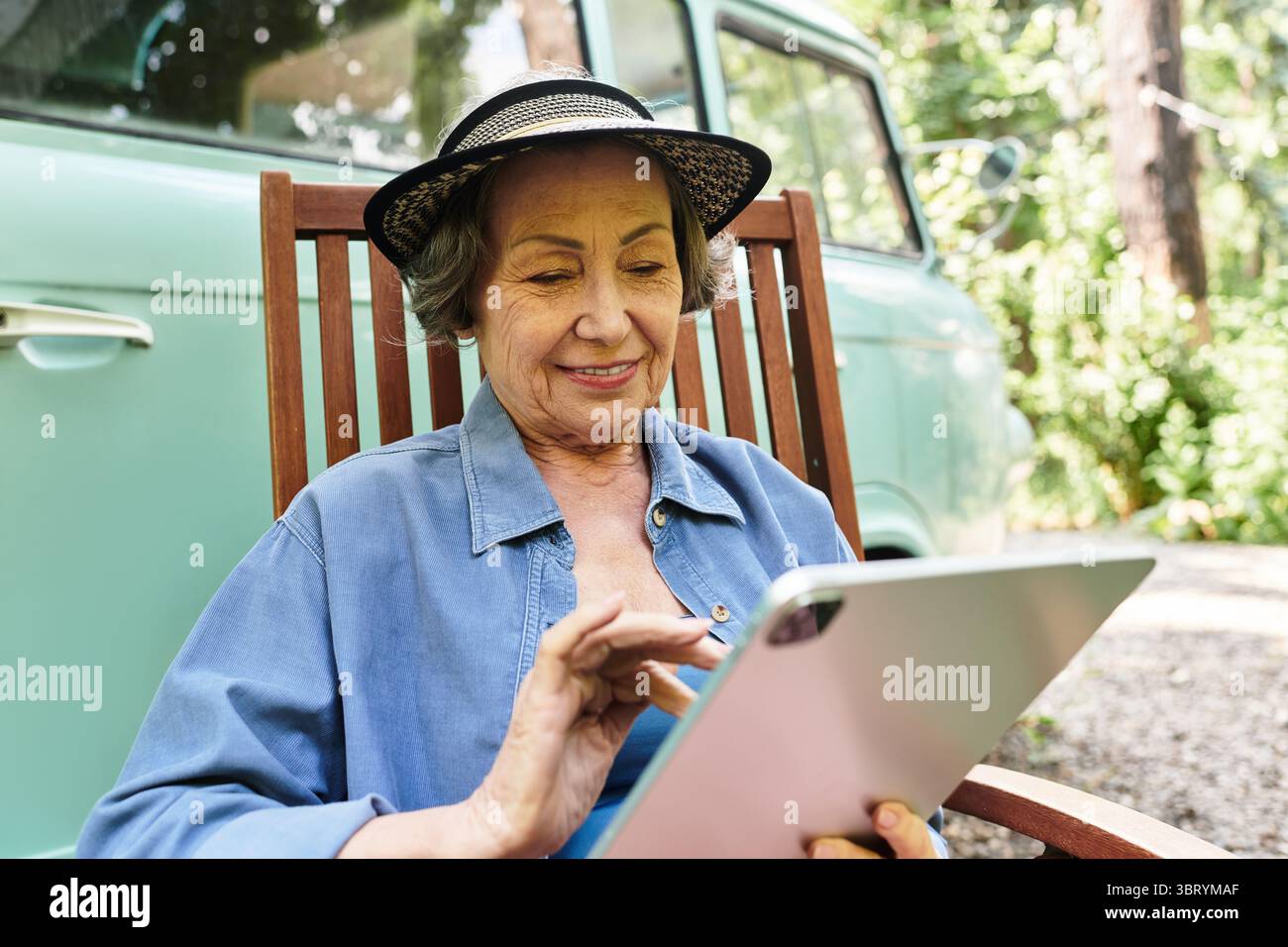 Seniorin entspannt sich im Garten mit einer Tablette und schätzt die Ruhe und Schönheit der Natur. Stockfoto