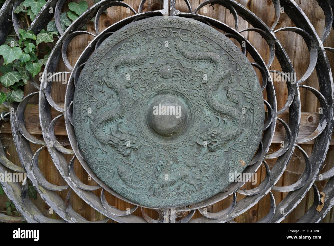 Dekoratives Metallschild mit kompliziertem Drachenmotiv und hölzernem Hintergrund. Dorking, England Stockfoto
