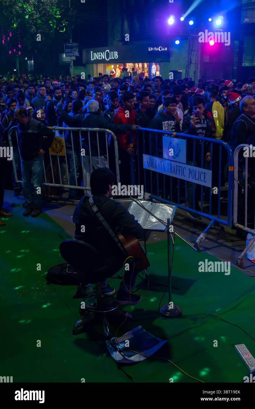 Kolkata, Westbengalen, Indien - 25.12.2018 : Straßensängerin singt festliche Stimmungslieder, während junge Menschen sich in der beleuchteten Park Street amüsieren. Stockfoto