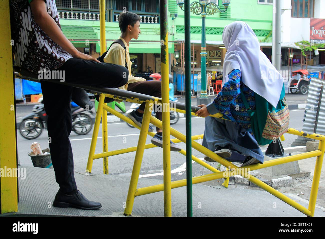 Die Studenten sitzen und warten auf öffentliche Verkehrsmittel an einem temporären Haltepunkt in der Malioboro-Straße. Stockfoto