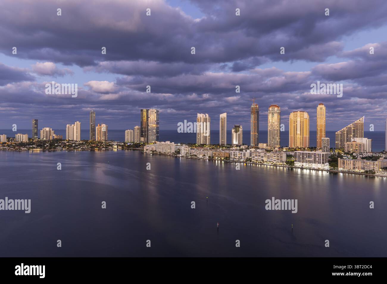 Blick aus der Vogelperspektive auf die atemberaubende Skyline, die sich im Wasser spiegelt, mit den hoch aufragenden Gebäuden von Sunny Isles Beach, beleuchtet vor dem Dämmerungshimmel, Sunny Isles Beach, Florida, USA. Stockfoto