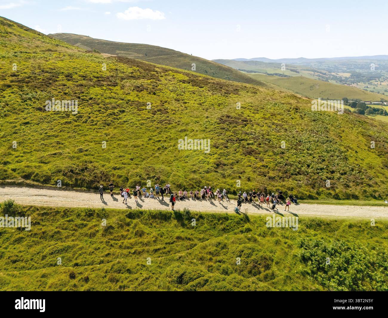 Eine Gruppe von Menschen läuft auf einem unbefestigten Pfad auf einem grasbewachsenen Hügel, möglicherweise wandern oder an einem Outdoor-Event teilnehmen, entlang des Bergweges towa Stockfoto