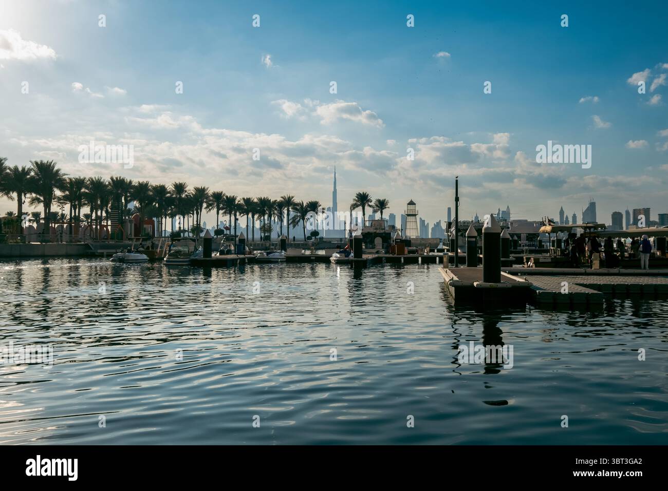 Dubai Immobilien Hintergrund mit Yachthafen am Wasser, Palmen und Blick auf die Skyline des Burj Khalifa über das Wasser bei Sonnenuntergang Stockfoto