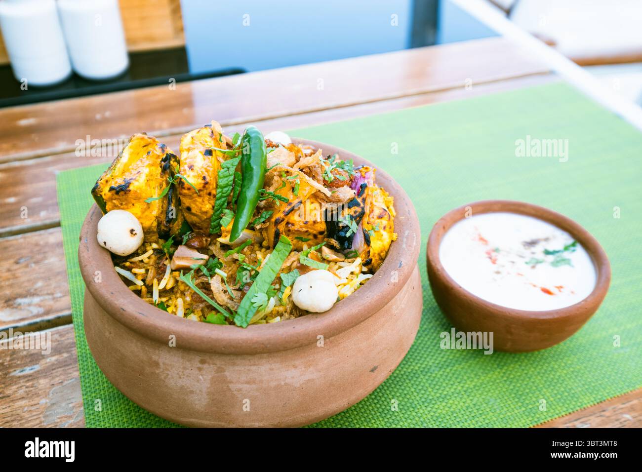 Paneer Tikka biryani in einem irdenen Topf mit Joghurt-Rita auf einem Tischset auf dem Tisch, indische Küche Lebensmittel fotografiert Hintergrund Stockfoto