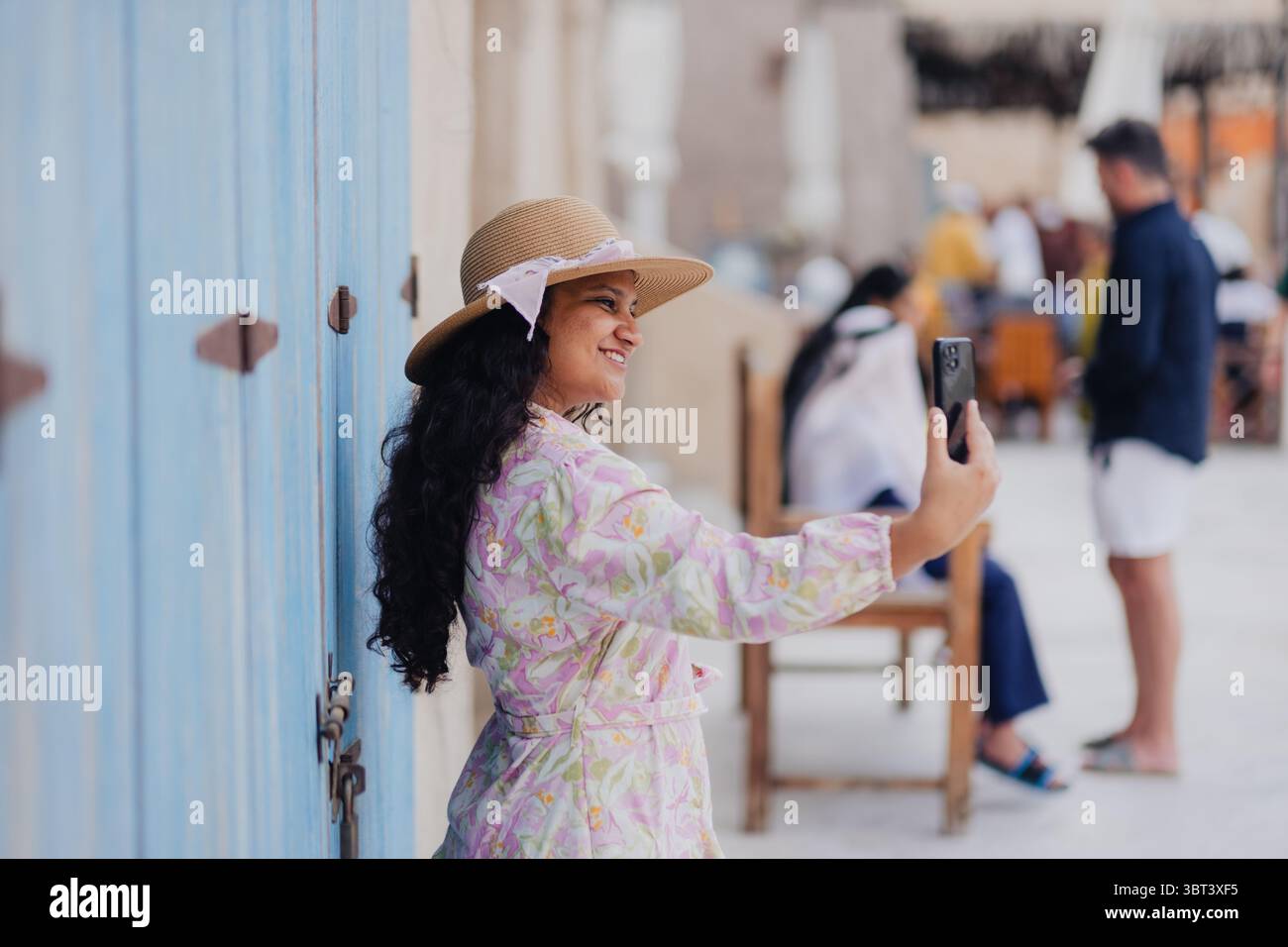 Junge Frau mit Strohhut und Blumenkleid, die Fotos in der historischen Gegend von Dubai macht, Stockfoto von Touristen, die im Al seef genießen Stockfoto