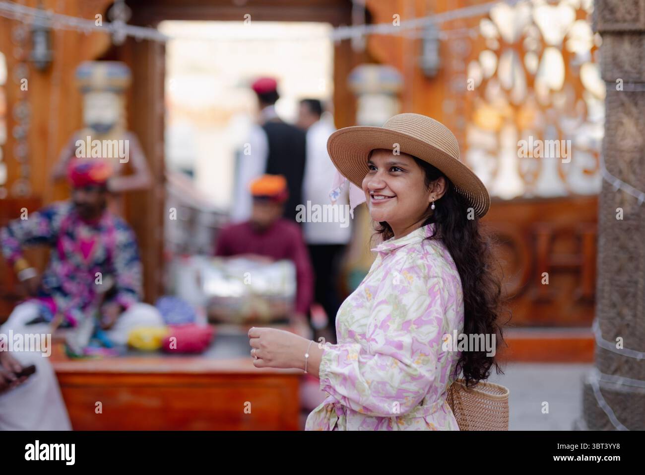 Eine junge Frau, die die kulturellen Straßen in Dubai erkundet, trägt einen Hut und ein Kleid mit ethnischem Muster Stockfoto