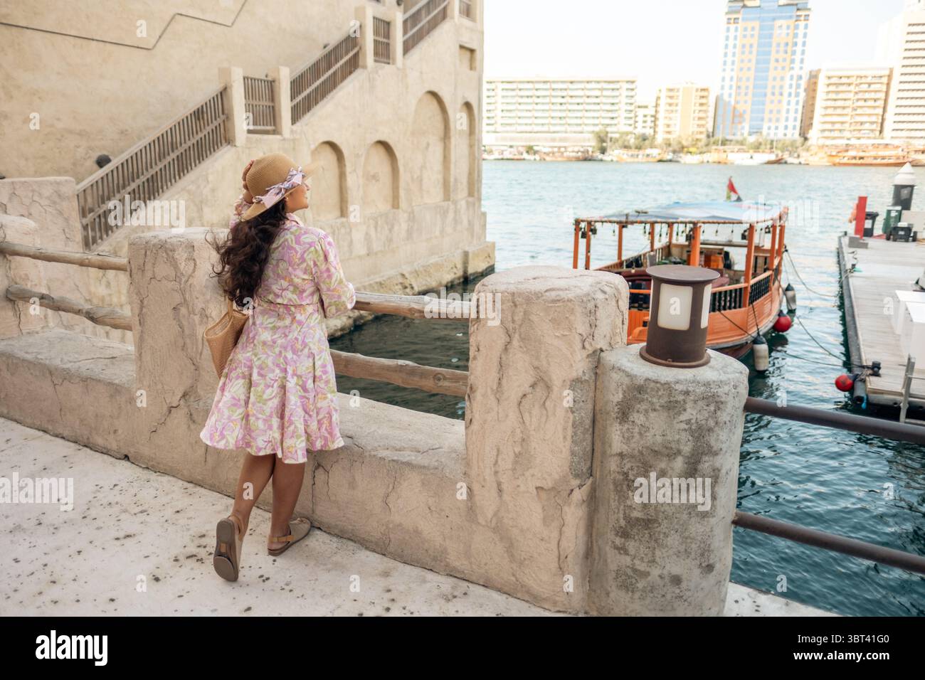 Junge südasiatische Frau in ethnischer Kleidung und Hut erkundet das historische Viertel Al Seef Creek in Dubai, umgeben von traditioneller Emirati Architektur Stockfoto