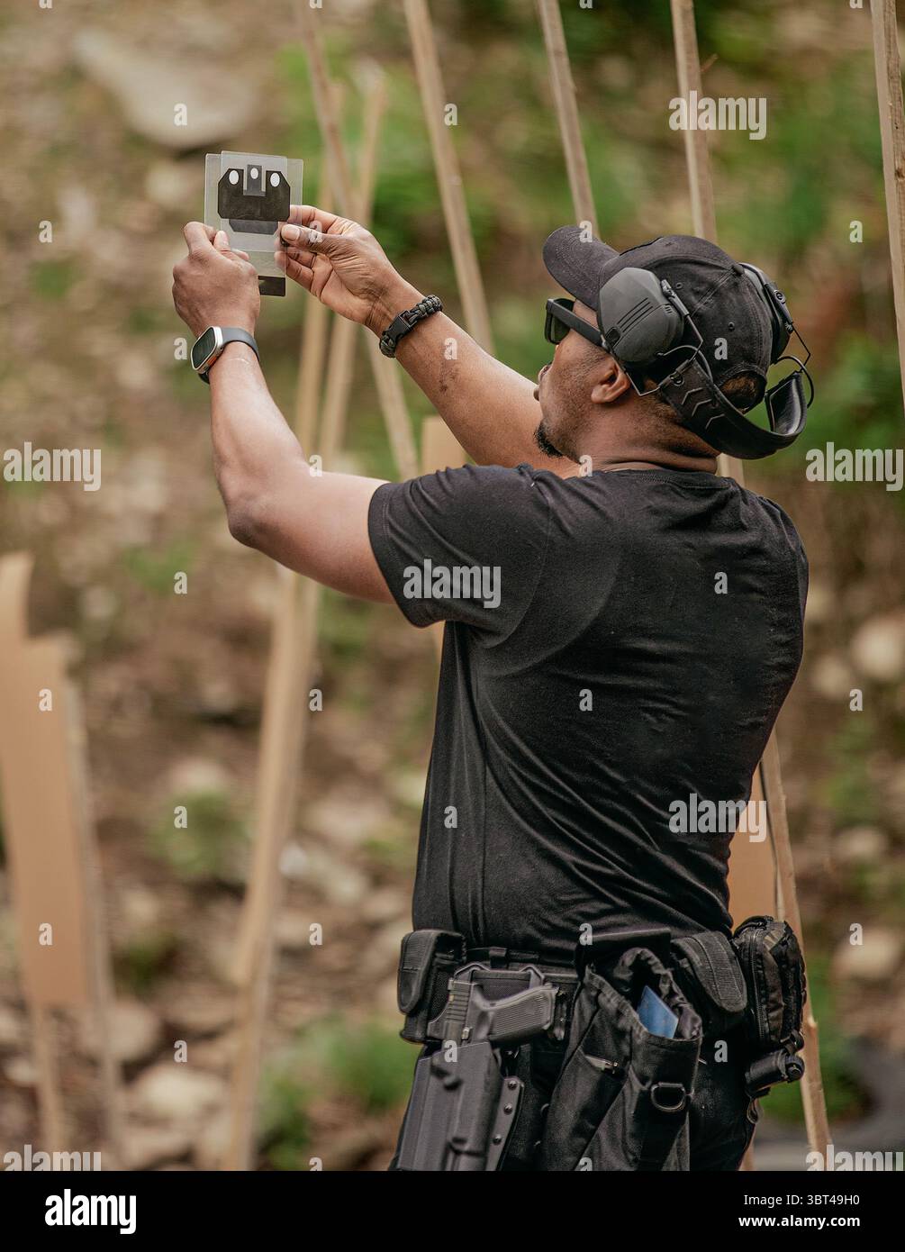Ein Schwarzer setzt ein Ziel, umgeben von einem verschwommenen äußeren Hintergrund. Er trägt Gehörschutz und verschiedene Gadgets und hält das Ziel fest Stockfoto