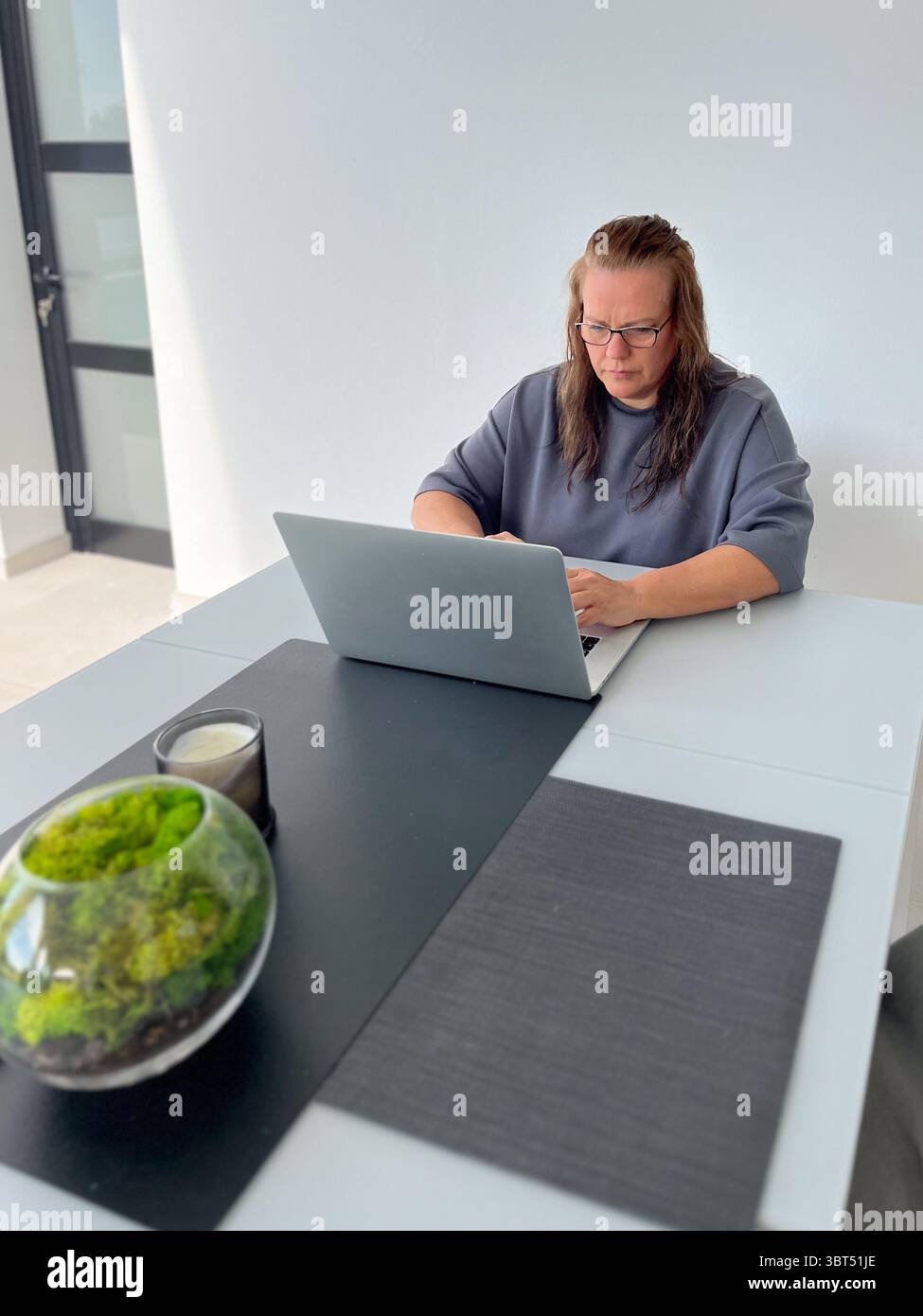 Weibliche Profi, die an einem eleganten Schreibtisch mit Laptop arbeiten, ergänzt durch eine Pflanze und Kerze, sorgt für eine ruhige und produktive Atmosphäre Stockfoto