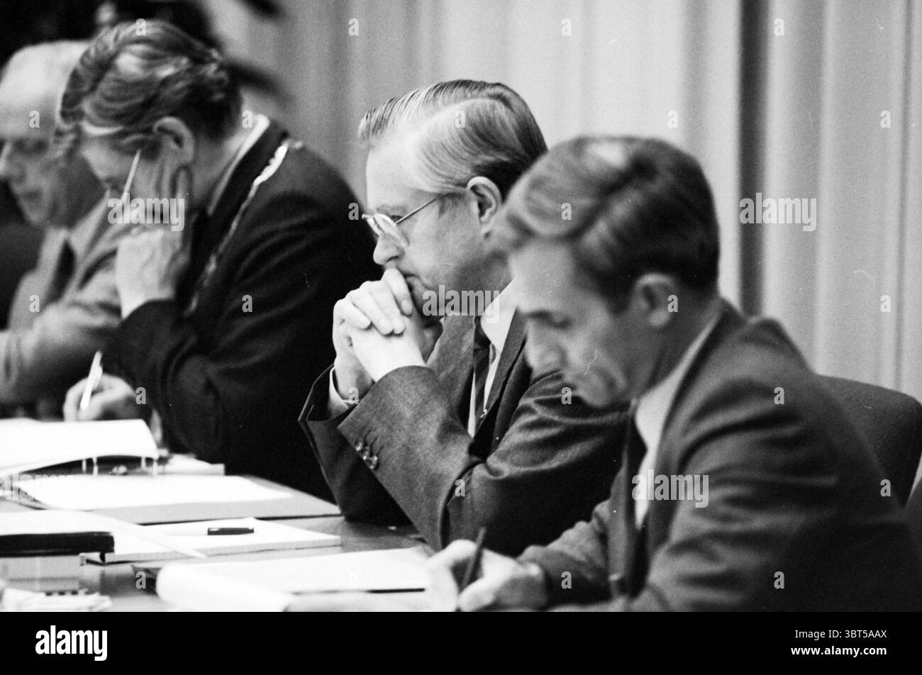 Budgettreffen Lisse Lisse Gemeinderat Lisse, Whizgle News, Dutch Desk, Niederlande, 1950 - 2000 am 29-10-1987. Dies sind die Themen im Bild. In einer formellen Umgebung sitzen vier Personen an einem langen Tisch und nehmen an einer ernsthaften Diskussion oder Besprechung Teil. Die Atmosphäre fühlt sich angespannt, aber konzentriert an und jeder Mensch ist tief in Gedanken. Die erste Person links ist ein älterer Mann, gekleidet in einem dunklen Anzug, mit grauen Haaren, die ordentlich nach hinten gekämmt sind, mit einer Brille, die das weiche Licht im Raum einfängt. Er neigt sich leicht nach vorne, zeigt einen Ausdruck von Konzentration, Finger s Stockfoto