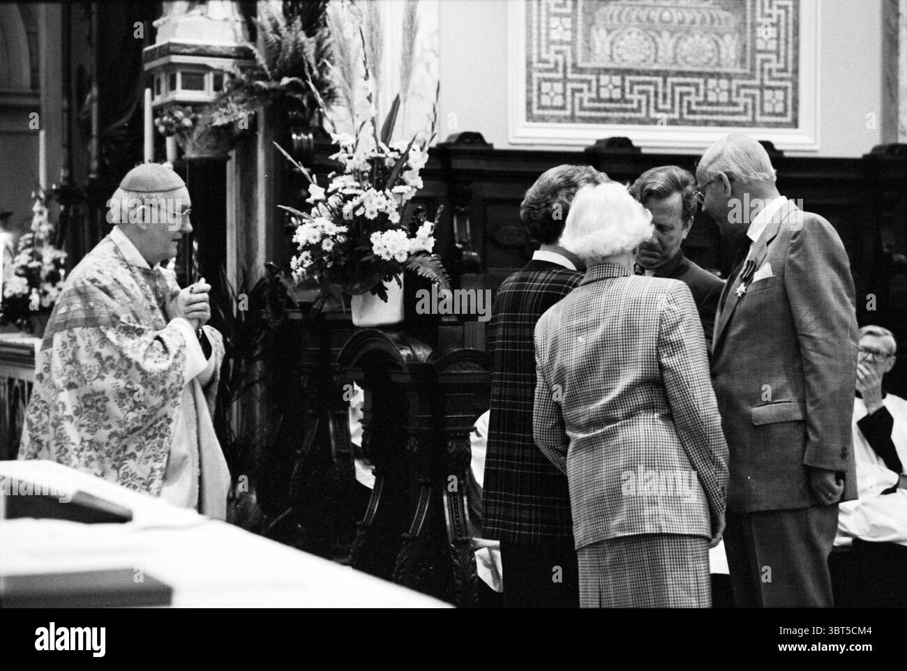 Auszeichnungen Joseph Church, Whizgle News, Dutch Desk, Niederlande, 1950 - 2000 am 15-05-1993. Das Bild enthält diese Themen. Die Szene zeigt ein religiöses oder zeremonielles Treffen in einem reich verzierten Innenraum, wahrscheinlich eine Kirche oder Kapelle. An der Spitze steht ein in traditionellen Gewändern gekleidetes Geistliches mit feierlichem Ausdruck. Seine Kleidung weist komplizierte Muster und Farben auf, die den zeremoniellen Charakter der Umgebung betonen. Um das Klerusmitglied herum befinden sich mehrere Personen, die ein kurzes, aufmerksames Gespräch führen. Sie scheinen in formeller Kleidung gekleidet zu sein, mit Anklängen gedämpfter Farben Stockfoto