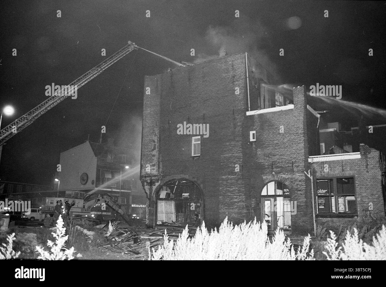 Fire Lido Houtplein Fire Fire Brigade Haarlem Houtplein the Netherlands, Whizgle News, Dutch Desk, Niederlande, 1950 - 2000 auf 30-07-1986. Dies sind die Themen im Bild. Die Szene zeigt eine nächtliche urbane Umgebung, die vom Chaos eines Feuers geprägt ist. Ein imposantes Backsteingebäude steht in einem Zustand der Not, mit sichtbaren Flammen oben und dickem Rauch, der in den dunklen Himmel strömt. Das Feuer erzeugt einen unheimlichen Glanz, der sich mit den umgebenden Schatten kontrastiert und die zerbröckelnde Fassade des Gebäudes beleuchtet. Eine hohe Leiter erstreckt sich von einem Feuerwehrwagen in Richtung der oberen Stockwerke des Gebäudes Stockfoto