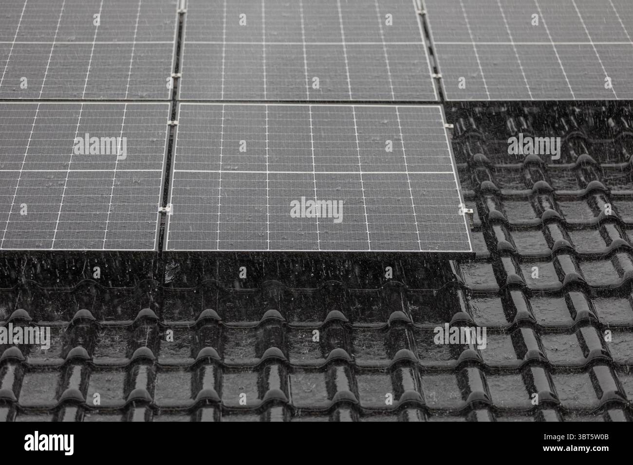 Unterkante der Installation von Solarpaneelen mit dunklen Dachziegeln und starkem Regen. Stockfoto