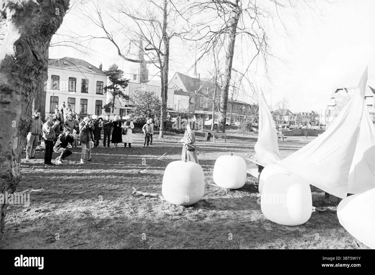 Enthüllung von Bildern in Hoftuin H'gom Unv, Whizgle News, Dutch Desk, Niederlande, 1950 - 2000 am 21-01-1990. Dies sind die Elemente im Bild. Die Szene bietet eine lebhafte Umgebung im Freien mit einer Mischung aus Menschen und künstlerischen Elementen. Im Vordergrund versammelt sich eine Gruppe von Zuschauern um eine zentrale Installation. Sie sind in verschiedenen Lagen gekleidet, was auf kühles Wetter hinweist. Mäntel, Tücher und Hüte verleihen der Szene Tiefe und Textur. Im Mittelpunkt steht eine große, weiße Stoffstruktur, möglicherweise eine Kunstinstallation, die sich sanft wie von einem sanften bree verfangen aufbläht Stockfoto