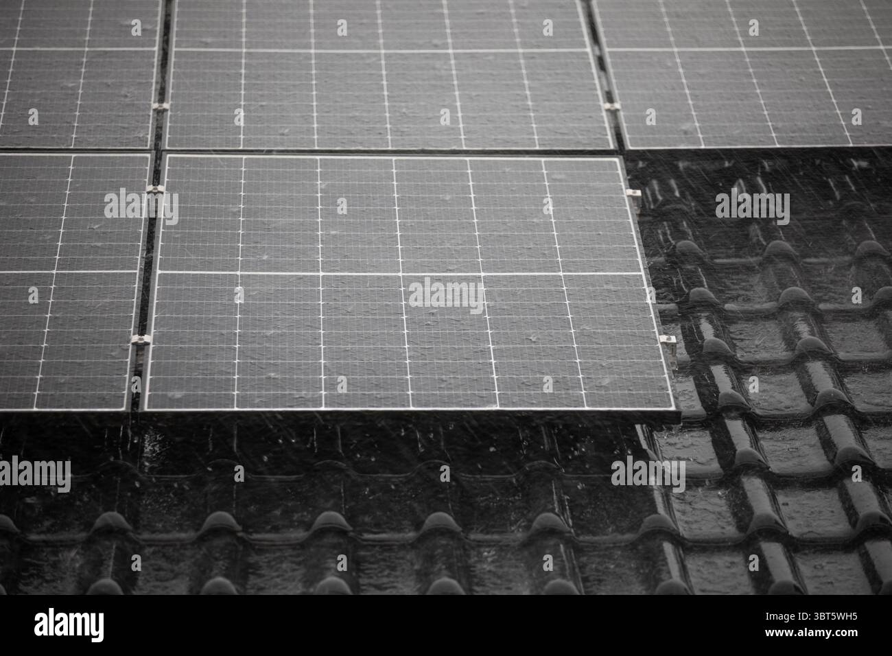 Solarpaneele und dunkle Dachziegel in landschaftlicher Ausrichtung unter starkem Regen. Stockfoto