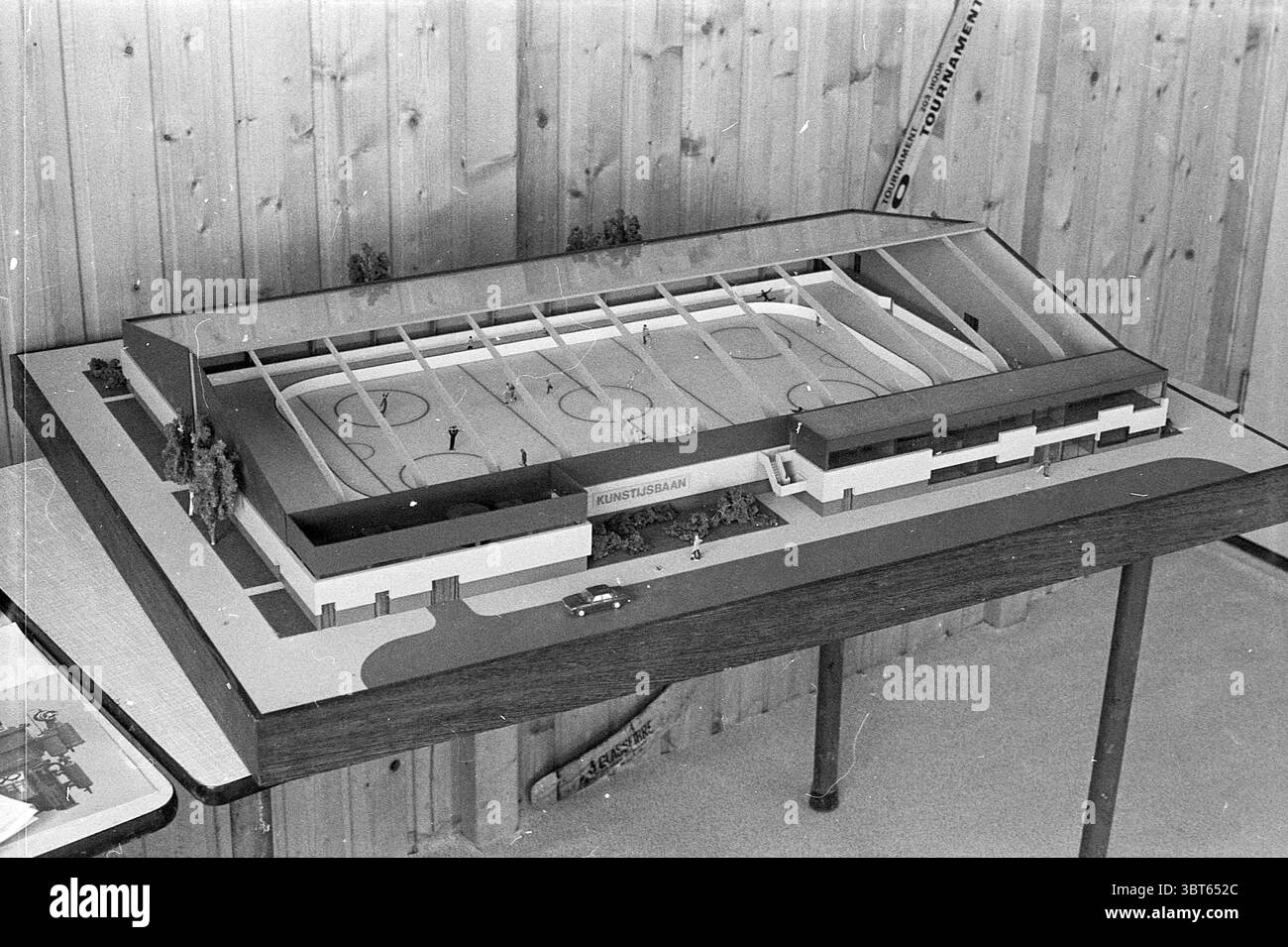 Model Ice Rink Ton Menken Leiden Model Ice Rink Eishockey, Whizgle News, Dutch Desk, Niederlande, 1950 - 2000 am 17-06-1976. Das Bild enthält diese Themen. Die Szene zeigt ein detailliertes Architekturmodell, das auf einer Tabelle angezeigt wird. Das Modell stellt eine Eishockeyarena dar und zeigt ein kompliziertes Design mit einer Skala, die eine umfassende Ansicht seiner Merkmale ermöglicht. Die Struktur der Arena ist überwiegend in weiß- und Grautönen gehalten, was eine moderne Ästhetik unterstreicht. Das Dach ist transparent und zeigt die darunter liegende Eisoberfläche, die mit einer glänzenden Oberfläche zur Simulation dargestellt ist Stockfoto