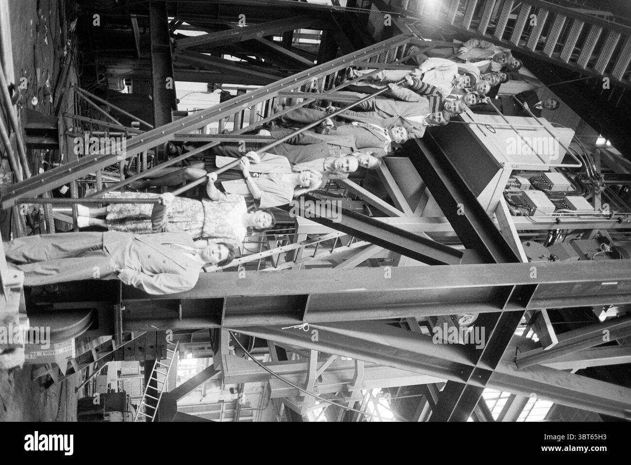 Gruppe von Russen bei Figee Haarlem, Niederlande, Whizgle News, Dutch Desk, Niederlande, 1950 - 2000 am 28.07.1993. Diese Themen sind in der Abbildung dargestellt. Die Szene zeigt eine Gruppe von Personen, die in einem großen industriellen Umfeld stehen und posieren. Die Architektur wird von schweren Metallkonstruktionen, darunter Balken und Treppenhäuser, dominiert. Diese Elemente erzeugen ein Raumgefühl, das aufgrund der zahlreichen sich kreuzenden Linien sowohl weitläufig als auch leicht klaustrophobisch ist. Die Menschen tragen Kleidung aus der Mitte des 20. Jahrhunderts, Männer in Anzügen und Krawatten und Frauen in Kleidern, die ein formelles As widerspiegeln Stockfoto