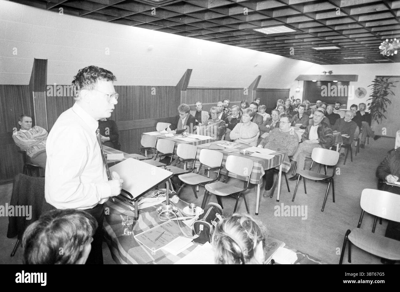 PvdA Treffen in Velserduin IJmuiden Labor Party PVDA IJmuiden Velserduinplein the Netherlands, Whizgle News, Dutch Desk, Niederlande, 1950 - 2000 am 08-12-1987. Diese Themen werden in der Abbildung angezeigt. In einem gut beleuchteten Innenbereich befinden sich zahlreiche Personen in Reihen von hellen Holzstühlen, die vor einem Lautsprecher angeordnet sind. Der Raum verfügt über ein bescheidenes Design mit einer Holztäfelung, die der Atmosphäre Wärme verleiht. Die Decke ist niedrig mit einem Gittermuster, was zu einer etwas gemütlichen, aber formellen Umgebung beiträgt. Vorne steht ein Mann, gekleidet in einem hellen Hemd und einer Brille. Er scheint engagiert zu sein Stockfoto
