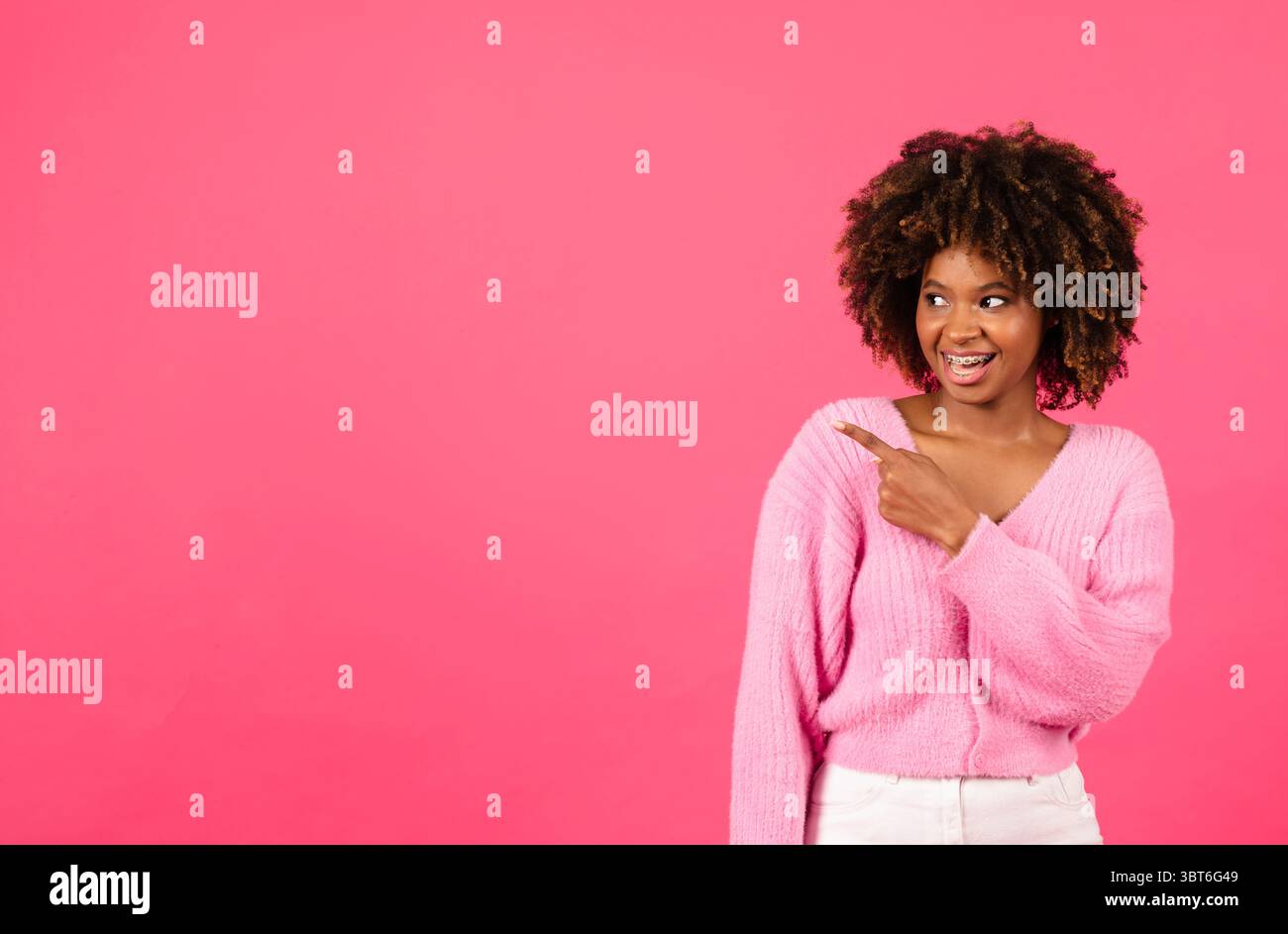 Lächelnde afroamerikanische Dame in ungezwungener Kleidung, offener Mund, Finger auf leeren Raum zeigen Stockfoto