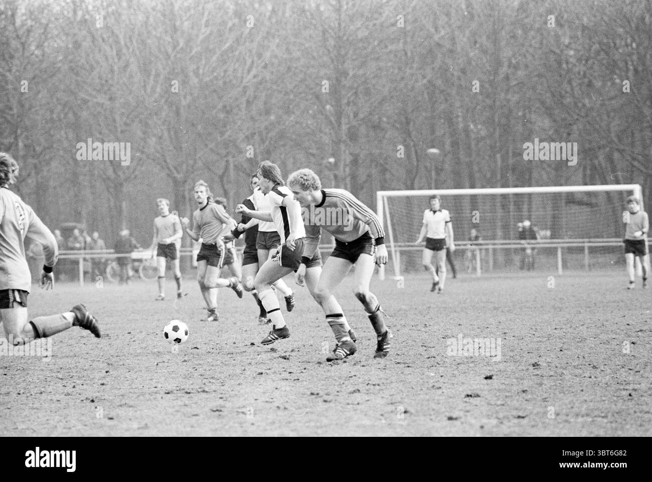 Energy - Kennemeren Football, Whizgle News, Dutch Desk, Niederlande, 1950 - 2000 am 07-04-1979. Dies sind die Themen im Bild. In dieser Szene entfaltet sich ein Fußballspiel auf einem grasbewachsenen Feld, das durch einen leicht bewölkten Himmel gekennzeichnet ist, der der Atmosphäre einen gedämpften, gräulichen Ton verleiht. Die Spieler tragen eine Mischung aus hellen und dunklen Trikots, wobei einige Shorts in Kontrast zur Einstellung stehen. Die Farbpalette ist überwiegend monochromatisch und besteht aus verschiedenen Grau- und Weißtönen, was das nostalgische Gefühl des Augenblicks unterstreicht. Die Spieler sind aktiv am Spiel beteiligt, mit einem Athleten Stockfoto