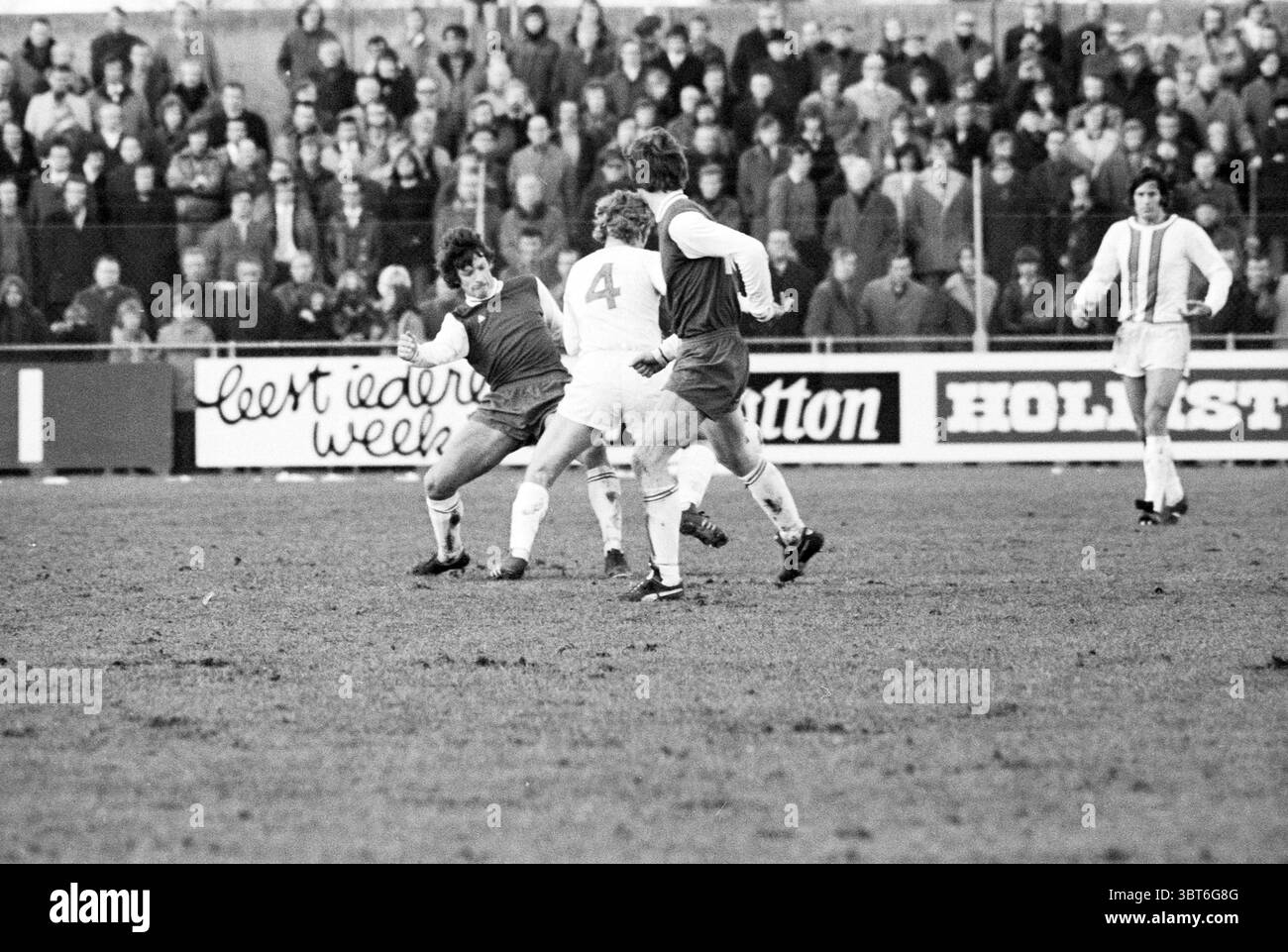 Football Match Haarlem-??., Whizgle News, Dutch Desk, Niederlande, 1950 - 2000. Diese Themen werden in der Abbildung angezeigt. Die Szene fängt einen intensiven Moment auf einem Fußballfeld ein, auf dem zwei Teams an einem Wettkampf teilnehmen. Im Vordergrund dribbelt ein Spieler, der ein dunkles Trikot mit einer numerischen Kennung trägt, gekonnt den Ball und navigiert zwischen zwei Gegnern in leichteren Trikots, einer mit der Zahl vier markiert. Die Ausdrucksformen der Spieler zeigen Entschlossenheit, während ihre dynamischen Körperpositionen Bewegung und Dringlichkeit nahe legen, während sie um die Kontrolle über den Ball kämpfen. Das Grasfeld ist A Stockfoto