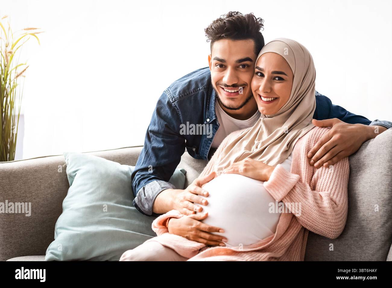 Schwangere muslimische Paar umarmt zu Hause, sitzen auf der Couch im Wohnzimmer Stockfoto