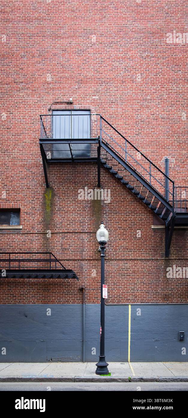 Blick auf ein rotes Backsteingebäude mit einer Metalltreppe für einen Außenausgang in der Nähe einer Straßenlaterne. Stockfoto