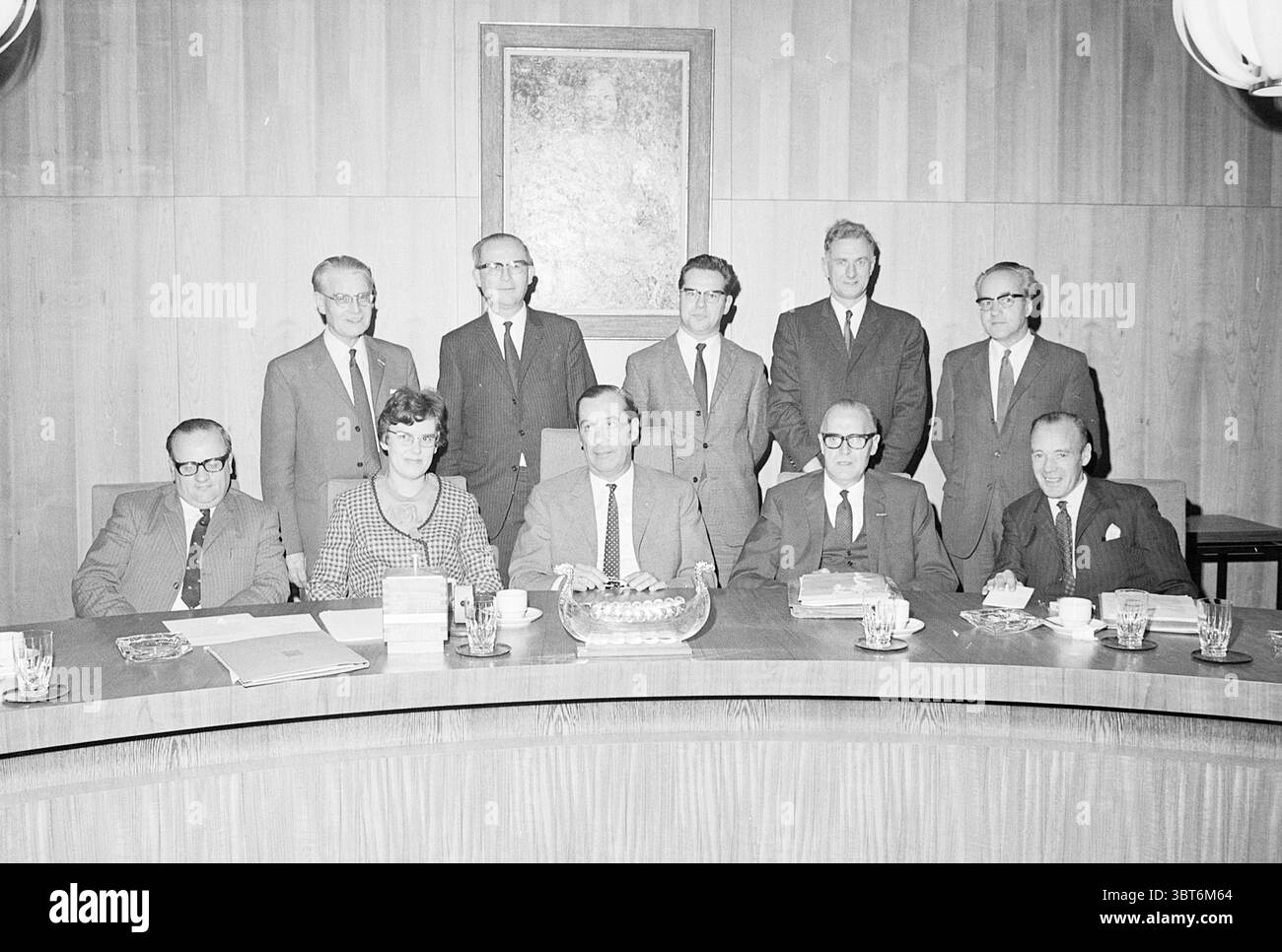 Installationskomitee Stadtfestlichkeiten Installation, Whizgle News, Dutch Desk, Niederlande, 1950 - 2000 auf 30-10-1969. Diese Themen sind in der Abbildung dargestellt. Die Szene zeigt eine Gruppe von Personen, die sich um einen großen, runden Konferenztisch versammelt haben. Insgesamt gibt es elf Personen, wobei eine Mischung aus Geschlechtern vertreten ist. Die Individuen tragen formelle Kleidung, die typisch für das Ende des 20. Jahrhunderts ist und viele Anzüge und Krawatten tragen, und die Frau vorne trägt ein gemustertes Kleid und eine Brille. Die Farbpalette ist stummgeschaltet und besteht größtenteils aus Grautönen, Braun und dunklen Tönen, die die er reflektieren Stockfoto