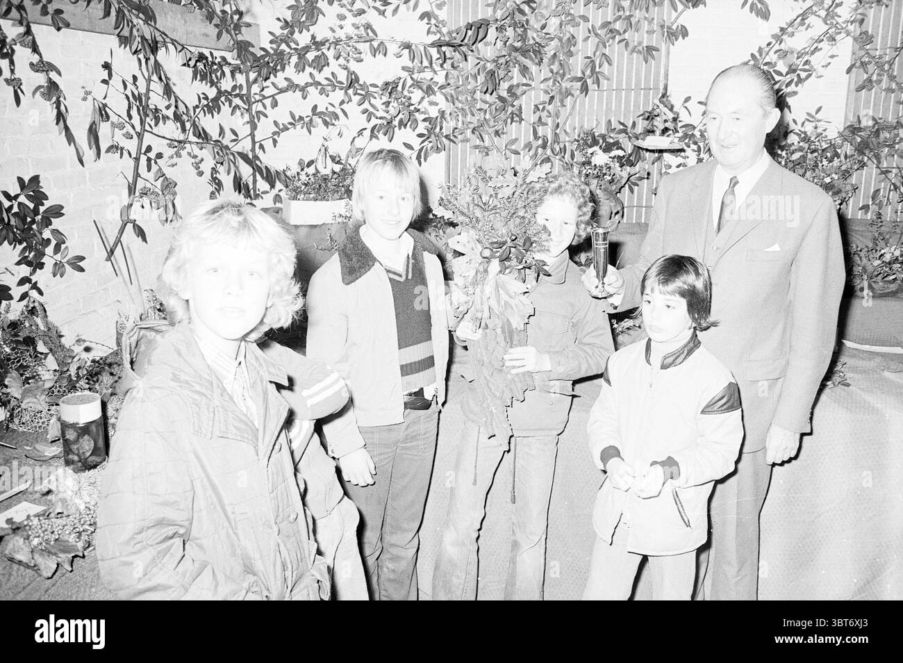 Herbstausstellung in Bloemendaal. Ausstellungen, Whizgle News, Dutch Desk, Niederlande, 1950 - 2000 auf 02-11-1974. Diese Themen sind in der Abbildung dargestellt. In einem lebhaften Innenbereich steht eine Gruppe von fünf Personen zusammen und strahlt ein Gefühl von Wärme und Kameradschaft aus. Der Hintergrund zeigt eine naturalistische Szene mit Grün, die auf eine Verbindung zur Natur oder vielleicht auf einen festlichen Anlass hindeutet. Die Beleuchtung ist weich, wahrscheinlich aus indirekten Quellen, wodurch ein sanftes Ambiente entsteht, das die Motive ohne scharfe Schatten hervorhebt. Ein subtiler Kontrast wird angezeigt, der verschiedene Grautöne hervorhebt, die ergeben Stockfoto