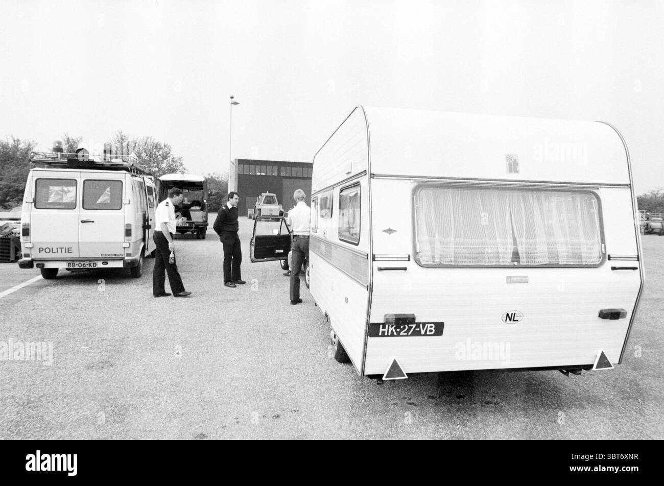 Caravan Control Nieuwe Meerdijk Caravan Control Badhoevedorp Nieuwemeerdijk, Whizgle News, Dutch Desk, Niederlande, 1950 - 2000 am 24-05-1985. Das Bild enthält diese Themen. Die Szene zeigt einen Parkplatz, der durch eine offene Asphaltfläche gekennzeichnet ist, mit Fahrzeugen gesäumt und von Bäumen im Hintergrund umgeben ist, die auf eine vorstädtische oder halbländliche Umgebung hinweisen. Im Vordergrund steht ein weißer Wohnwagen oder Anhänger, dessen Äußere unter natürlichem Licht leuchtet. Der Caravan ist klassisch eingerichtet und verfügt über leicht getönte Fenster, die einen Hauch von Inneneinrichtung freigeben. Daneben Stockfoto
