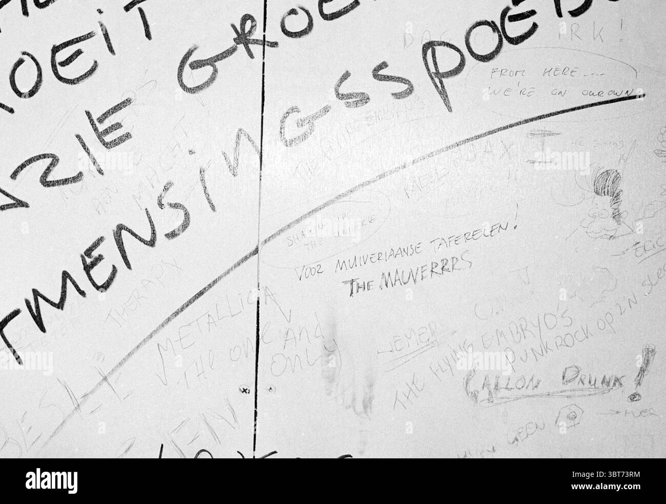 Slogans Toilette Cafe Long Gentleman, Whizgle News, Dutch Desk, Niederlande, 1950 - 2000 am 01-04-1993. Diese Themen sind in der Abbildung dargestellt. Die Szene verfügt über eine strukturierte Wand, die als Hintergrund dient und eine Vielzahl von Markierungen und Beschriftungen zeigt. Die Oberfläche scheint verwittert und robust zu sein, was darauf hindeutet, dass sie seit einiger Zeit an Ort und Stelle ist. Die vorherrschenden Farben sind gedämpft, wobei Grau- und Weißtöne die Palette dominieren, was ein wenig industrielles Flair vermittelt. Verschiedene handgeschriebene Wörter und Sätze sind über die Oberfläche verstreut. Diese Inschriften variieren in Größe und Stil, einige sind b Stockfoto