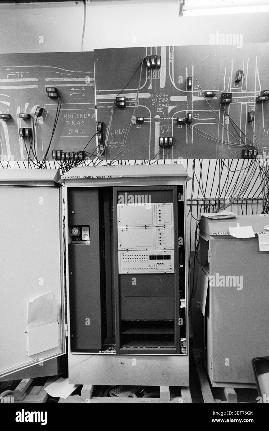 Computer zur Steuerung von Ampelmaschinen von Haarlem the Netherlands, Whizgle News, Dutch Desk, Niederlande, 1950 - 2000 am 21-03-1979. Dies sind die Elemente im Bild. Die Szene präsentiert einen technischen Arbeitsbereich, der von einer Vielzahl von Maschinen und Verkabelungen dominiert wird. Im Vordergrund befindet sich ein großer Metallschrank, dessen Oberfläche eine polierte, leicht reflektierende Oberfläche aufweist. Der Schrank ist teilweise geöffnet und zeigt ein organisiertes Inneres mit verschiedenen elektronischen Komponenten, einschließlich Leiterplatten und Kabeln. Auf der linken Seite ist eine blassweiße Seitenverkleidung partiall Stockfoto
