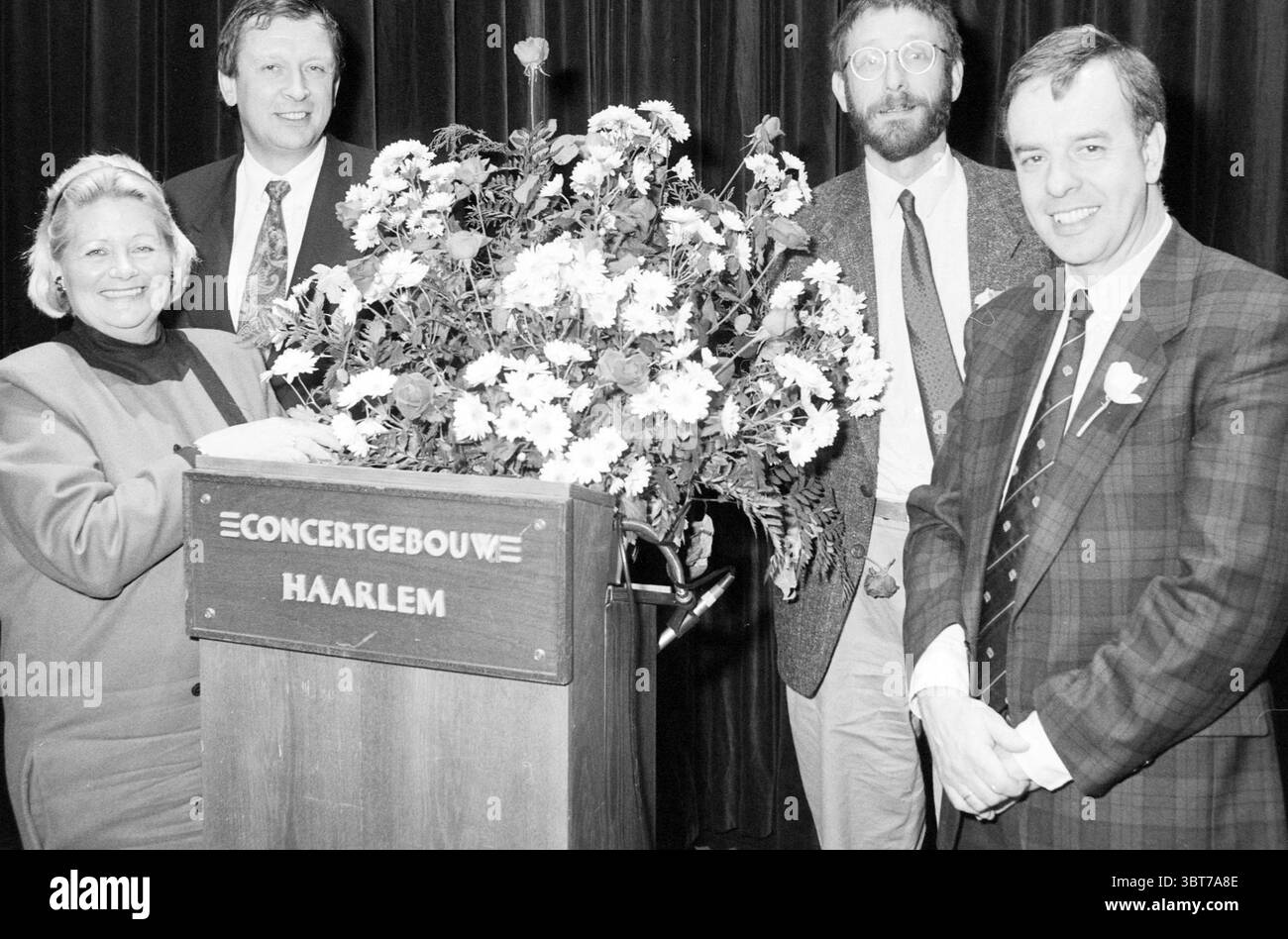 Sitzung im Concertgebouw Haarlem Promotion Foundation Präsentation der Werbe-Pin an Derk Snoep Direktor des Frans Hals Museums Haarlem Niederlande, Whizgle News, Dutch Desk, Niederlande, 1950 - 2000 am 14-02-1991. Das Bild enthält diese Themen. In einem belebten Innenbereich stehen vier Personen um ein lebhaftes Blumenarrangement gruppiert, das auf einem Podium sitzt. Der Blumenstrauß ist üppig und voller Blumen in weiß-, Gelb- und Lila-Tönen, die der Szene einen lebendigen Touch verleihen. Die erste Person links ist eine Frau mit kurzen, gestylten Haaren, die Selbstvertrauen ausstrahlt Stockfoto