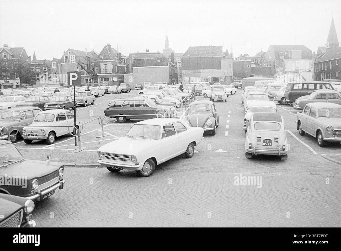Parkplatz, Whizgle News, Dutch Desk, Niederlande, 1950 - 2000 auf 10-1967. Diese Themen sind in der Abbildung dargestellt. Die Szene zeigt einen belebten Parkplatz mit einer Vielzahl von Autos aus verschiedenen Epochen, hauptsächlich Modelle aus der Mitte des 20. Jahrhunderts. Die Fahrzeuge, die in Grau-, weiß- und gedämpften Pastelltönen lackiert sind, schaffen eine nostalgische Atmosphäre, die eine längst vergangene Zeit widerspiegelt. Im Vordergrund steht ein kleines weißes Auto, das schräg zwischen einer Gruppe anderer Fahrzeuge geparkt ist. Um ihn herum sind mehrere Kleinwagen und Kombiwagen in ordentlichen Reihen angeordnet, einige zeigen Alterspuren, wie z. B. Stockfoto
